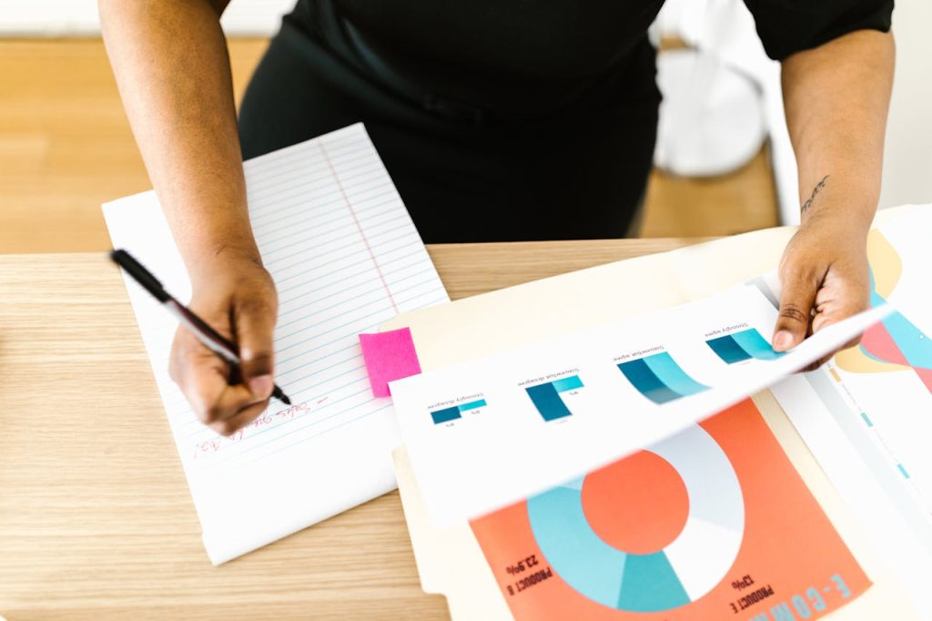 Businesswoman writing notes while analyzing printed graph reports at a desk.